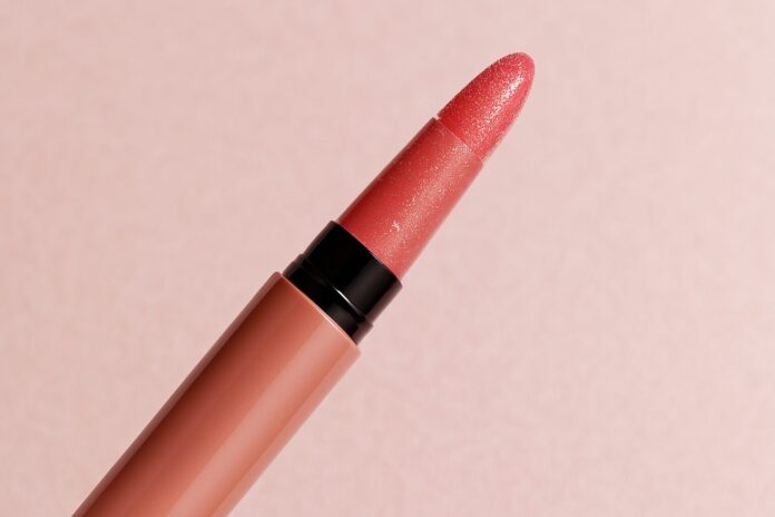 Nahaufnahme eines eleganten Lipgloss-Stifts mit roséfarbenem Glanz und Applikator vor pastellrosa Hintergrund im Querformat